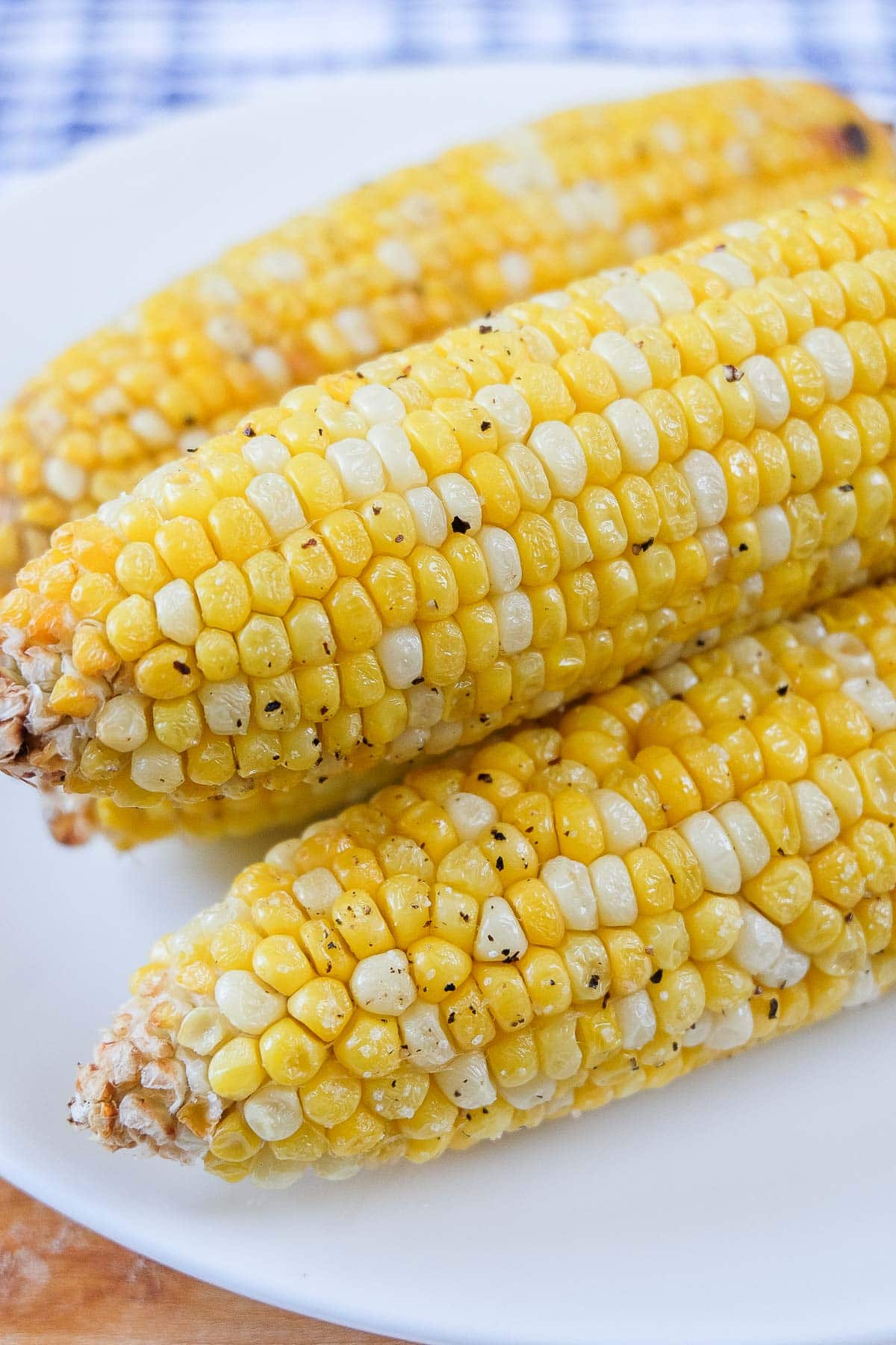 cooked corn on the cob on white plate with blue cloth behind