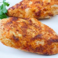 cooked chicken breast with red spices on white place with parsley