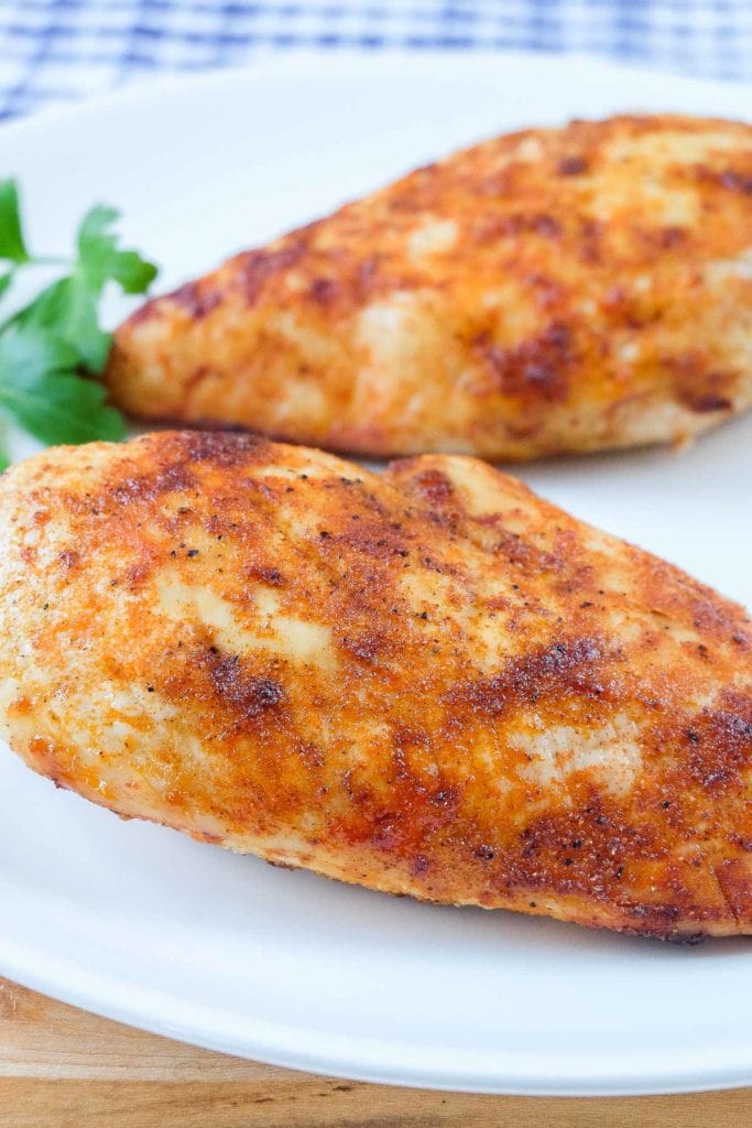 spiced cooked chicken breasts on white plate with parsley