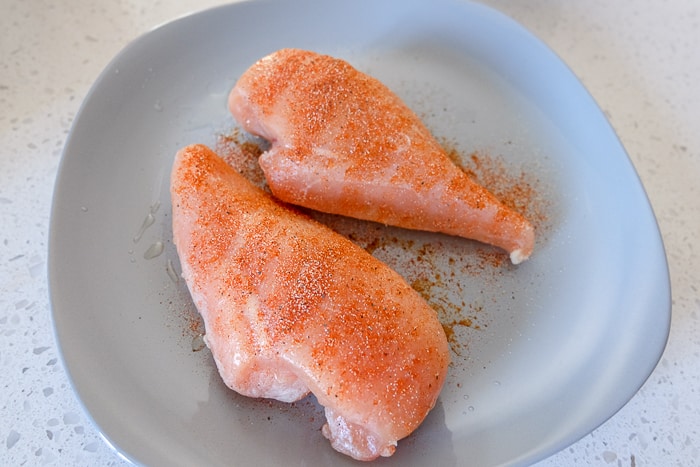 frozen chicken breast covered in spices on grey plate