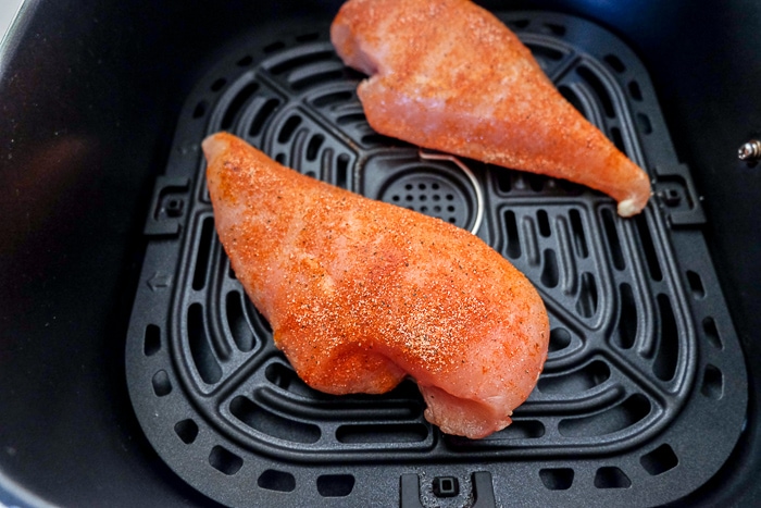 frozen chicken breasts sitting on black air fryer tray with spices on top