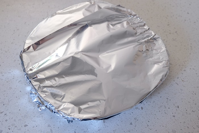plate of chicken with tin foil over top on white counter top