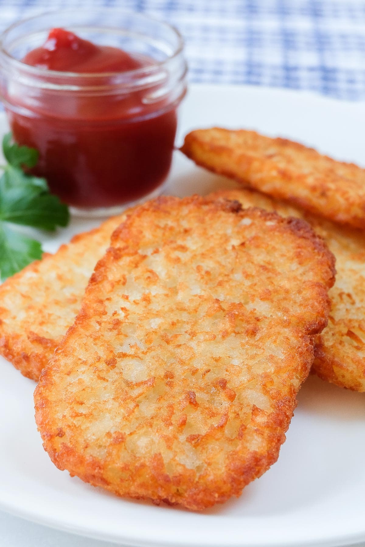 crispy golden brown hash brown patties on white plate with ketchup behind