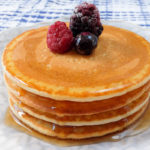 stack of pancakes on plate with berries on top and syrup