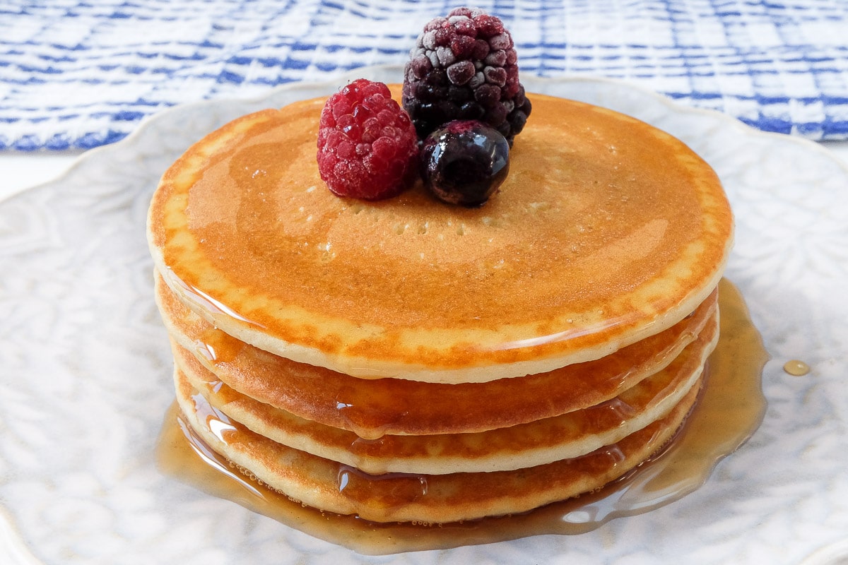 stack of pancakes on plate with berries on top and syrup