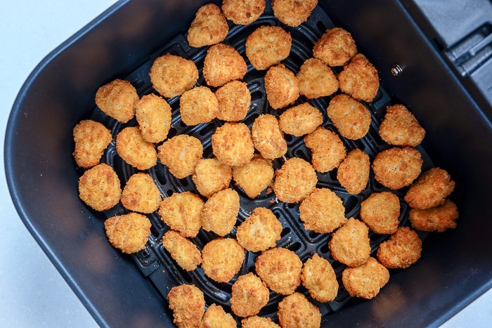 cooked popcorn chicken in black air fryer tray on counter