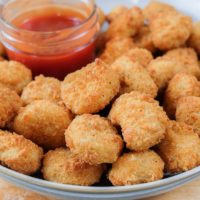 crispy breaded popcorn chicken in a bowl with dipping sauce behind