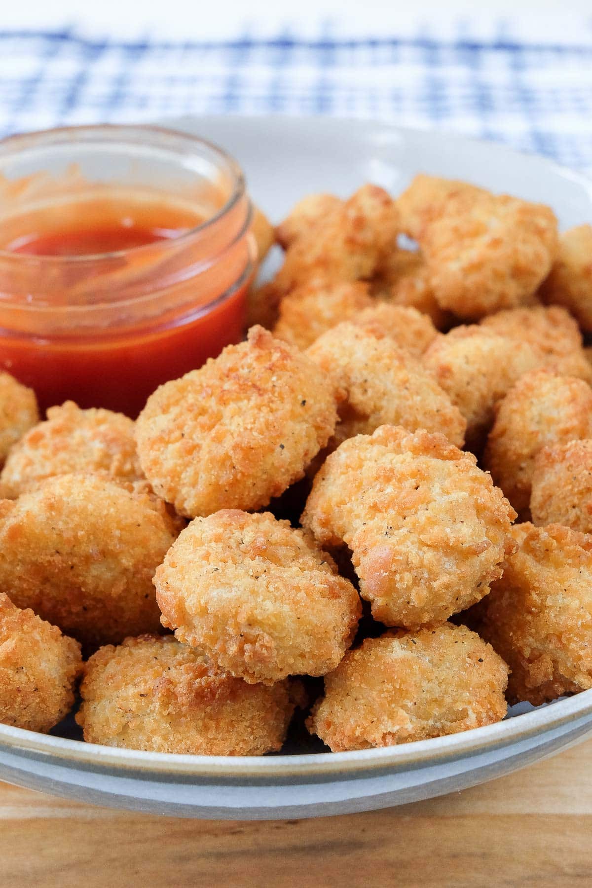 crispy popcorn chicken in bowl with dipping sauce and blue cloth behind