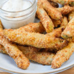 crispy breaded pickles in bowl with white dipping sauce behind