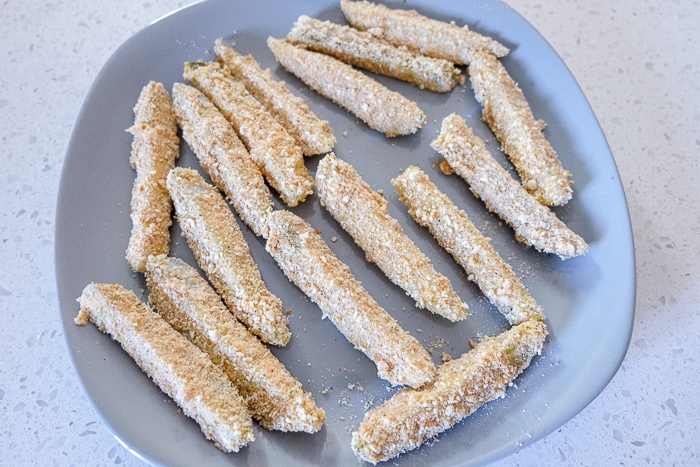 breaded raw pickle spears on grey plate on counter top