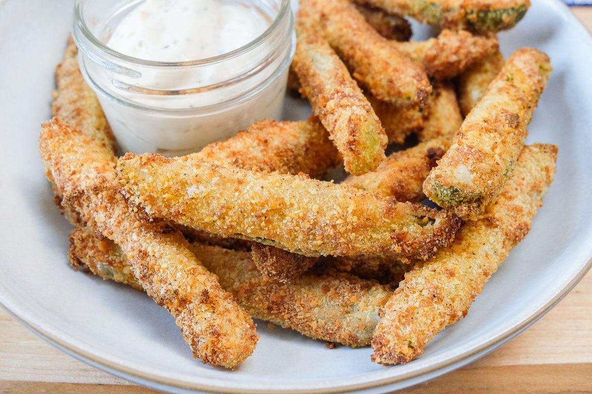crispy breaded pickles in bowl with white dipping sauce behind