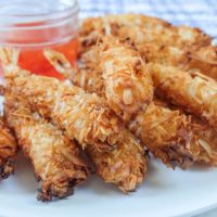crispy cooked coconut shrimp with red dipping sauce on white plate