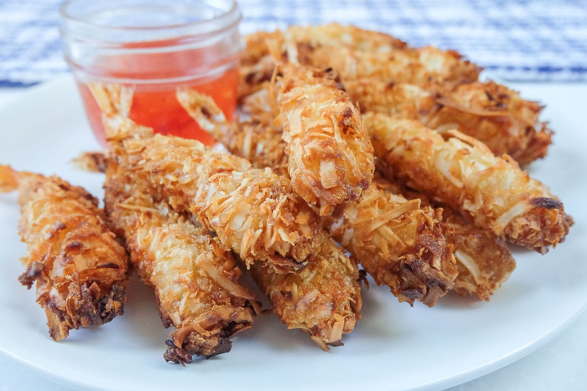 crispy cooked coconut shrimp with red dipping sauce on white plate