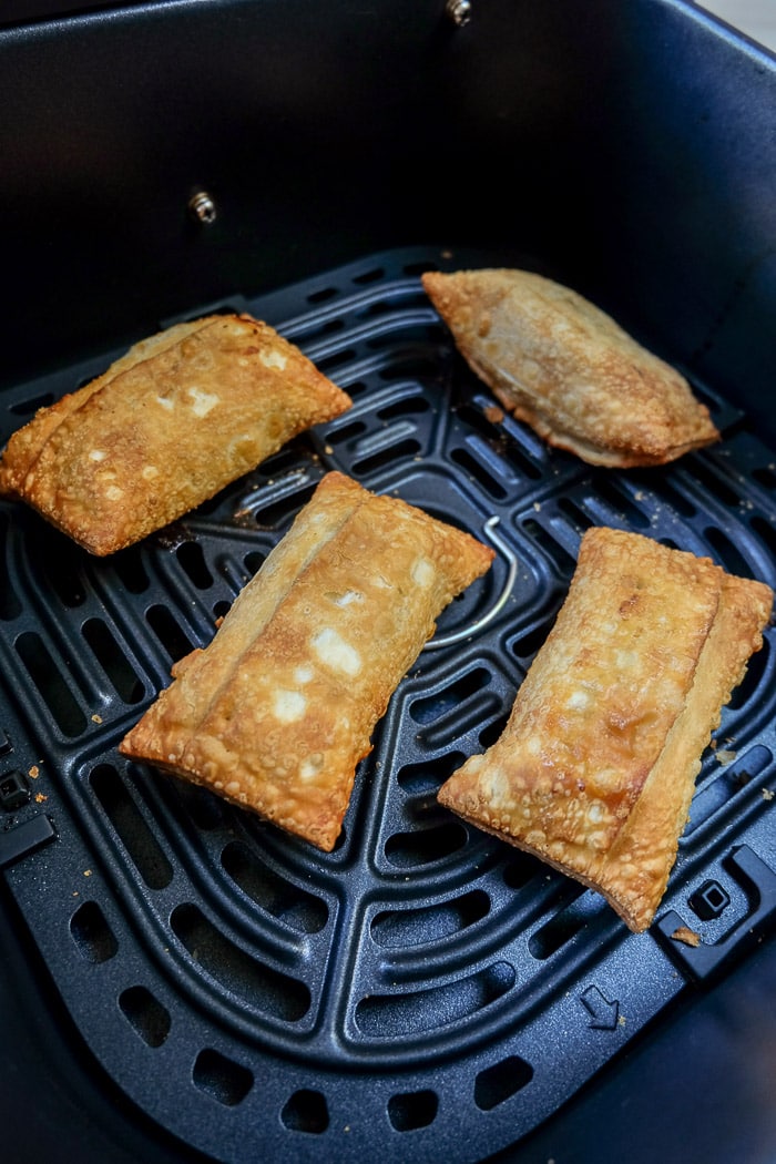 cooked egg rolls in a black air fryer tray