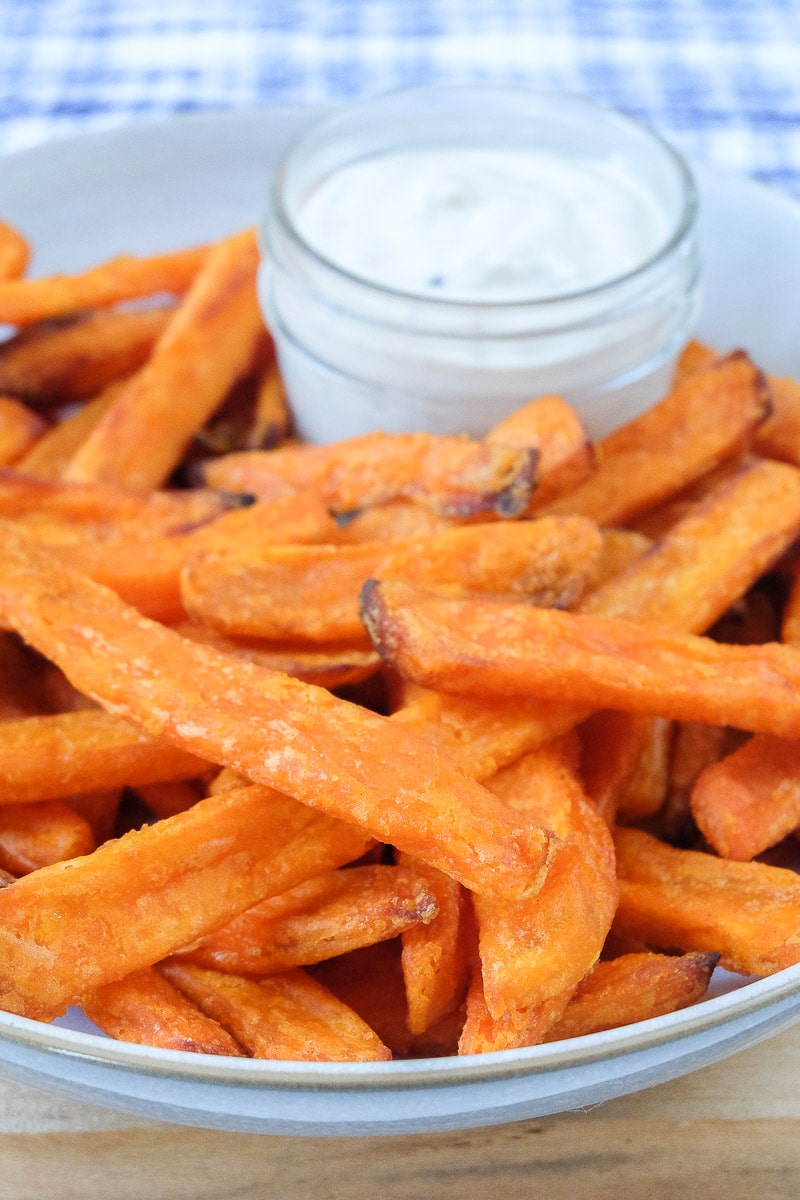 orange crispy sweet potato fries in bowl with white dipping sauce behind