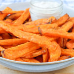 crispy orange sweet potato fries in bowl with white dipping sauce behind