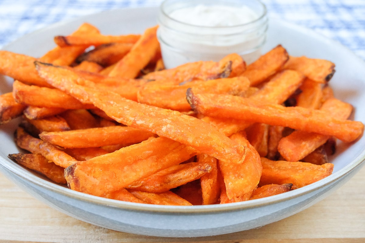 crispy orange sweet potato fries in bowl with white dipping sauce behind