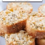 air fried pieces of baguette with garlic, herbs and cheese stacked on plate and text overlay "air fryer garlic bread"