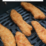 breaded chicken strips in black air fryer basket with text overlay "frozen chicken strips in the air fryer".