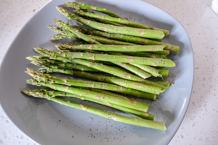 trimmed asparagus on blue plate with seasoning on top