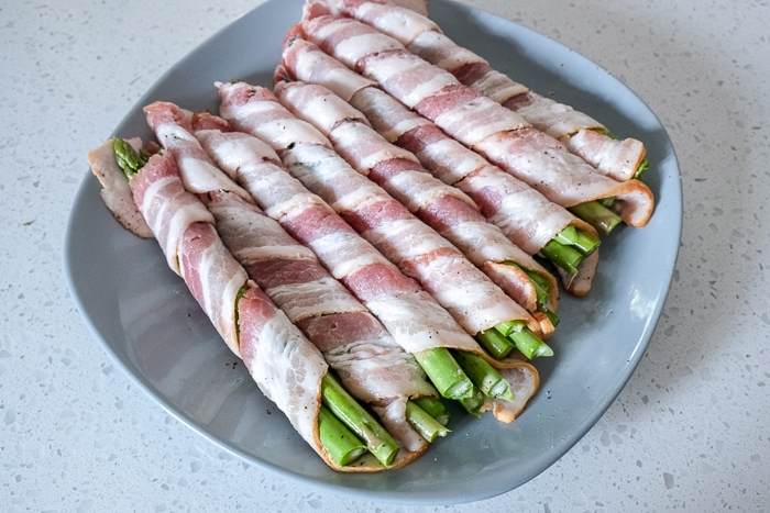 raw bacon wrapped around asparagus on blue plate on white counter
