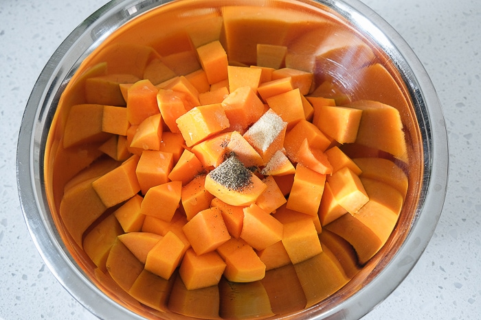 silver bowl of raw butternut squash with spices on top unmixed