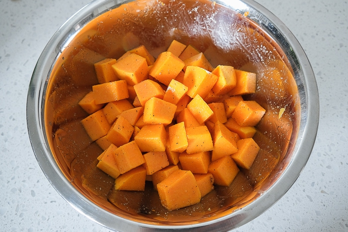 silver bowl with raw cubed butternut squash on white counter top