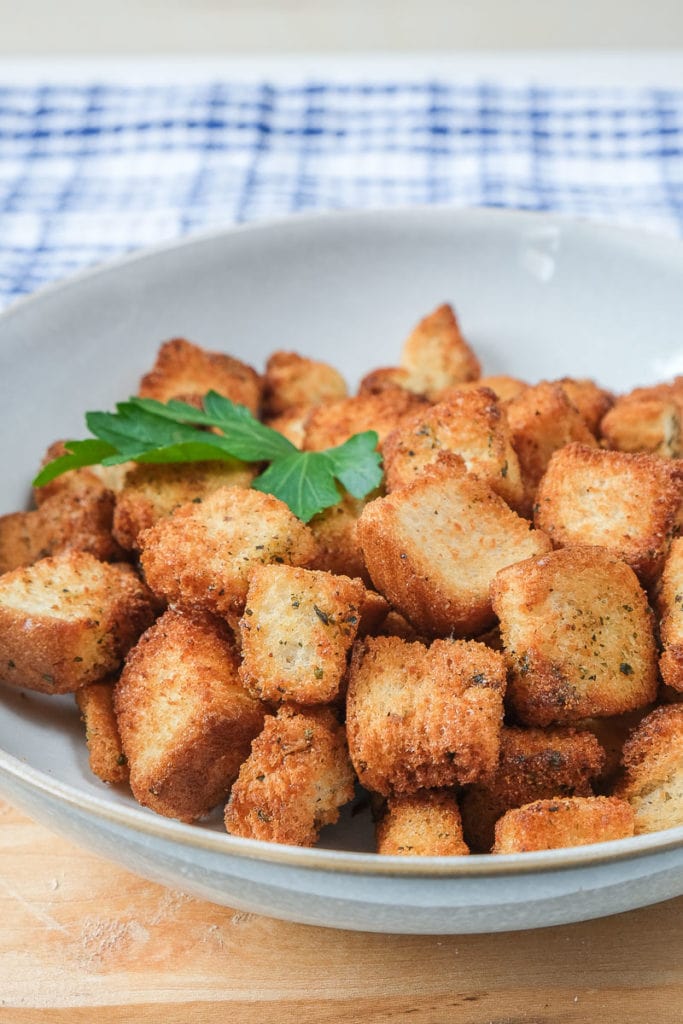 crispy croutons in bowl on wooden plank with blue cloth behind