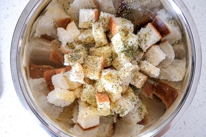 white bread pieces in silver mixing bowl with butter and spices