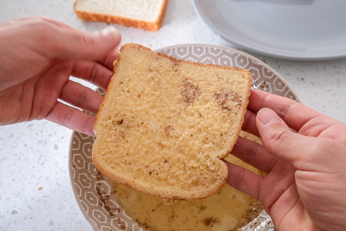 egg soaked bread held in hands above bowl on counter