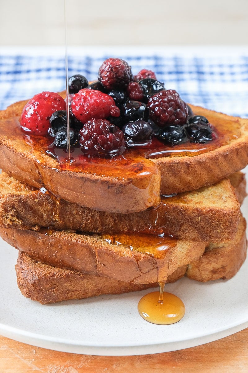 crispy french toast in a stack on plate with berries and syrup on top