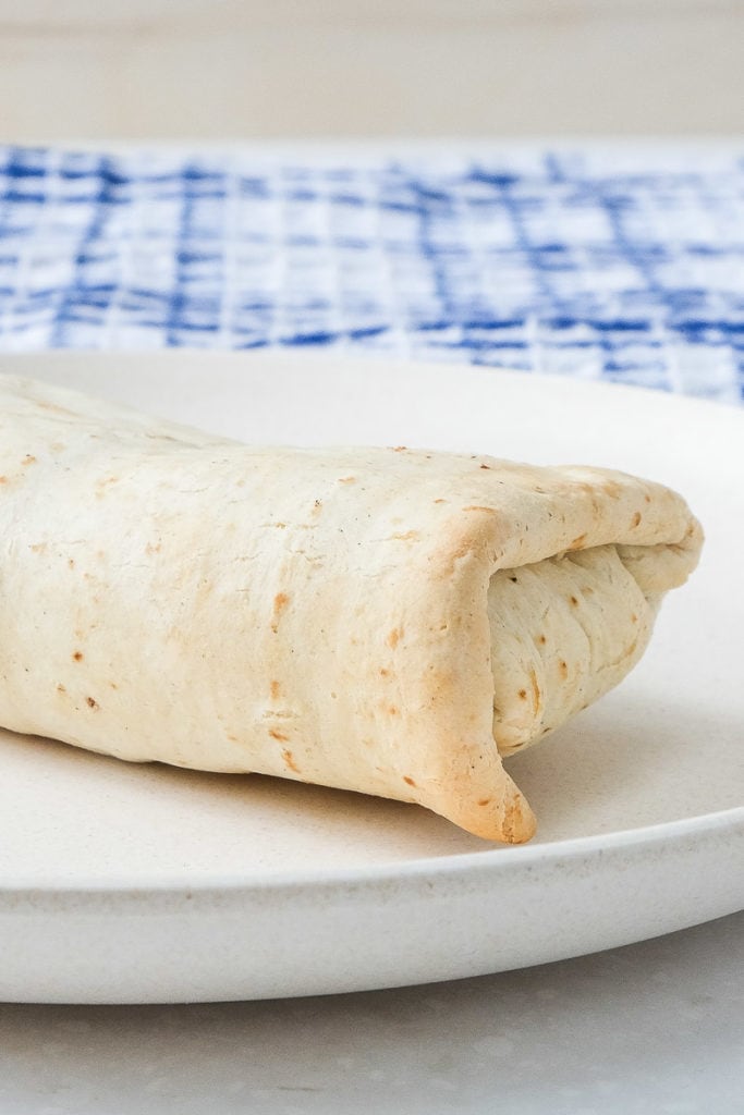 cooked burrito on white plate with blue towel behind