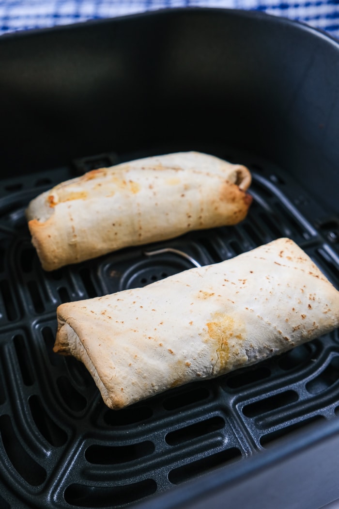 cooked burritos in black air fryer tray on counter