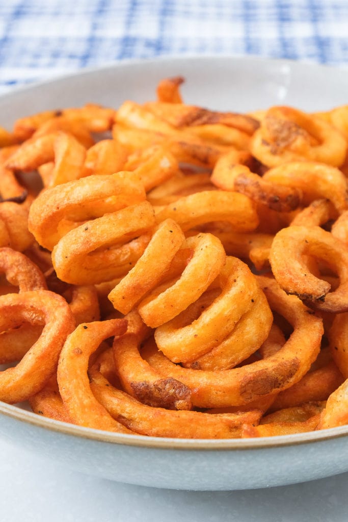 crispy orange curly fries in a bowl with blue towel behind