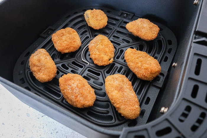 frozen jalapeno poppers in black air fryer tray on white counter