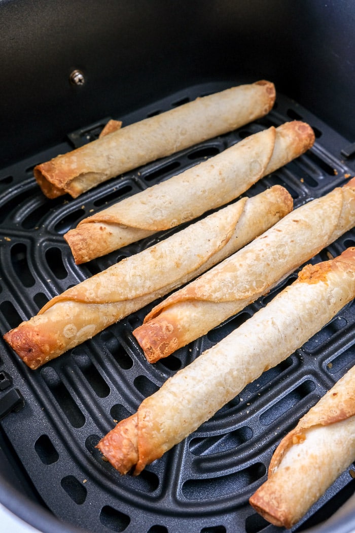 cooked taquitos in black air fryer tray