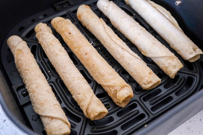 frozen taquitos in black air fryer tray on white counter
