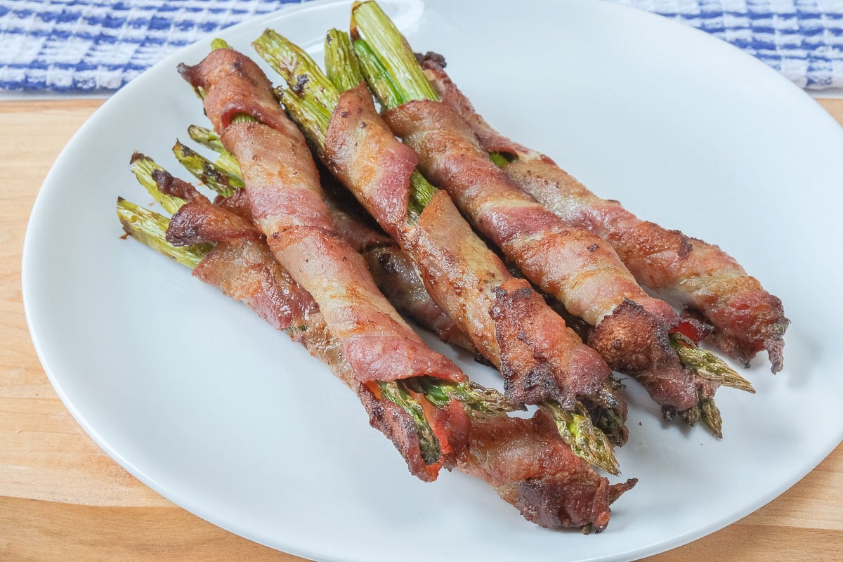 bacon wrapped asparagus on white plate on wooden board