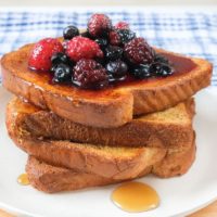 stack of french toast on white plate with berries and syrup on top