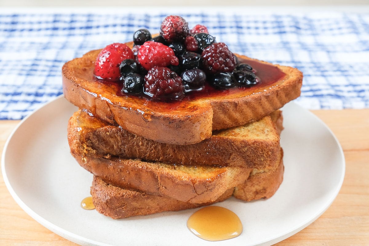 stack of french toast on white plate with berries and syrup on top