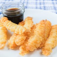 crispy shrimp tempura laying on white plate with soya sauce for dipping behind