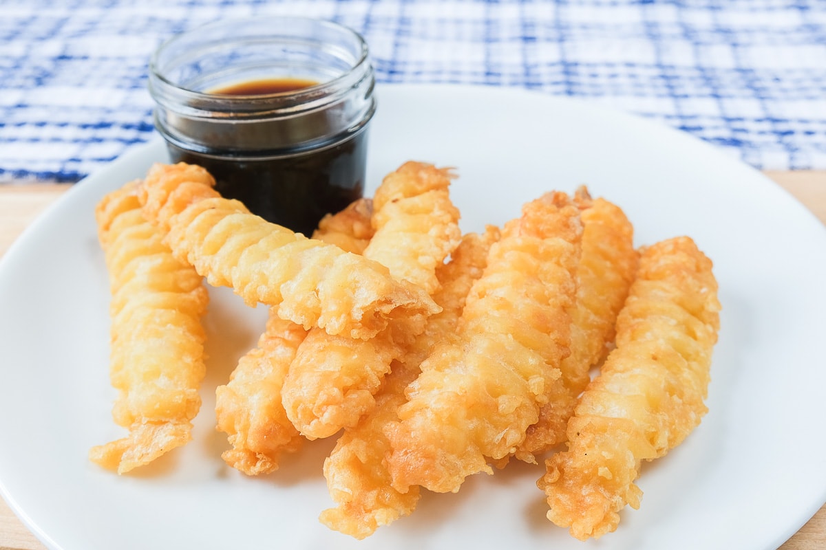 crispy shrimp tempura laying on white plate with soya sauce for dipping behind