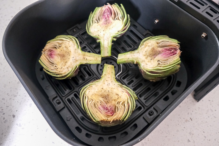 artichoke halves in black air fryer tray on white counter top