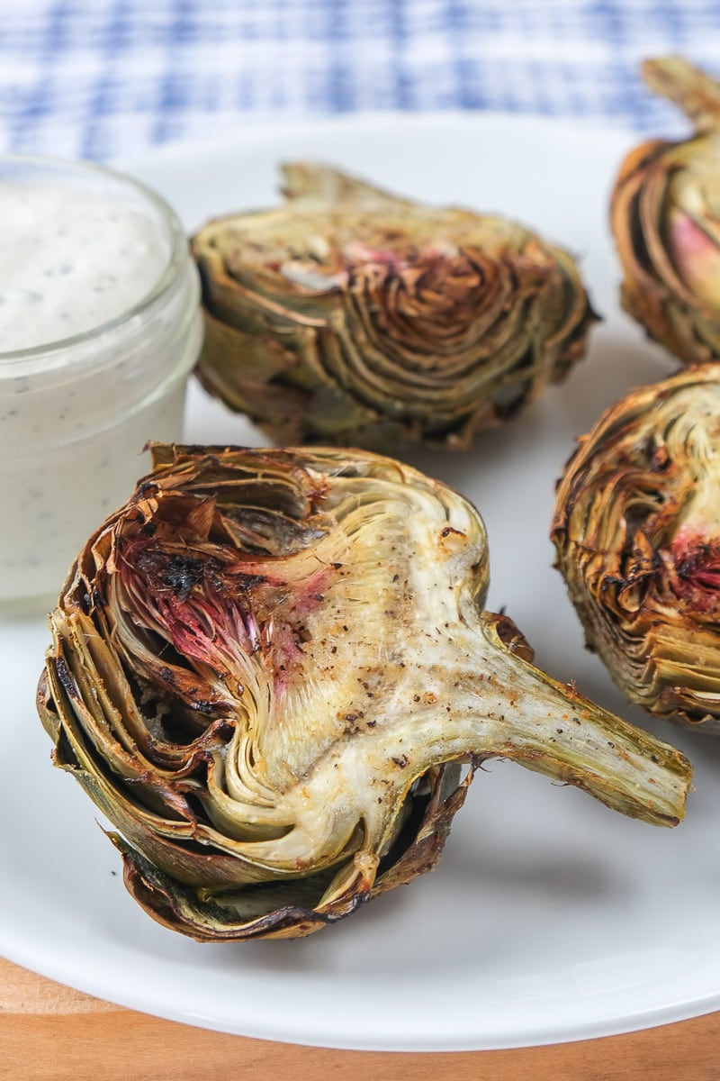 cooked artichokes on white plate with dip beside