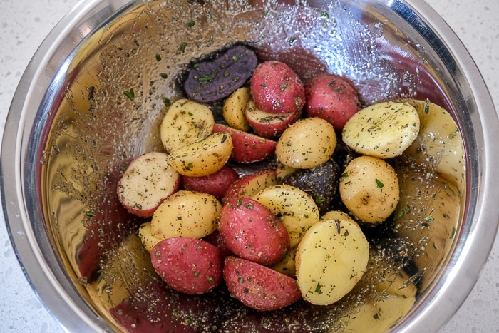halved baby potatoes covered in spices in silver mixing bowl