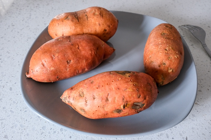 raw sweet potatoes on grey plate on white counter