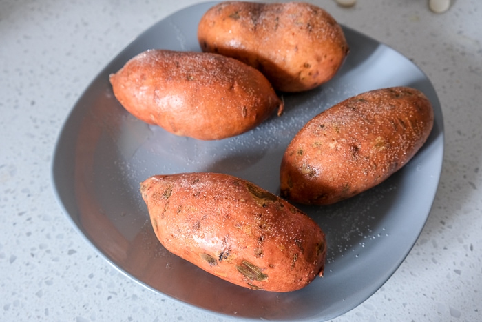salt covered raw sweet potatoes on grey plate on white counter top