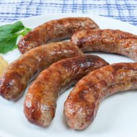 bratwurst sausages on white plate with mustard beside