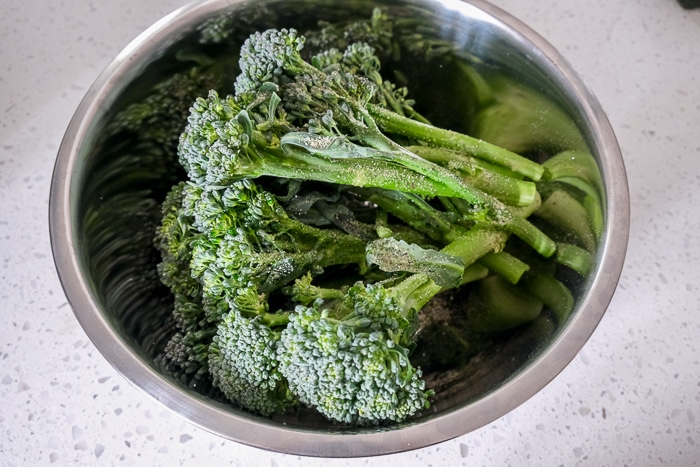 broccolini in silver bowl on white counter coated with spices