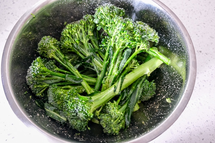 cut broccolini in silver bowl coated in oil and spices